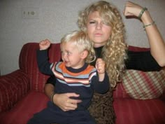 a woman sitting on top of a red couch next to a boy with blonde hair