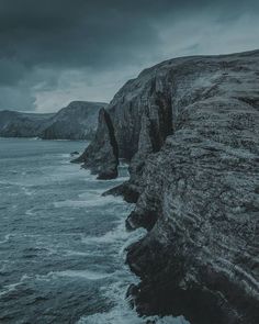 an ocean view with dark clouds over the water and cliffs on either side that are rocky