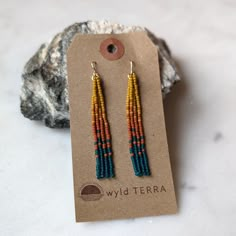 the beaded earrings are on display in front of a rock and paper tag that says wild terra