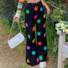 a woman standing in front of some flowers holding a white bag and wearing black pants