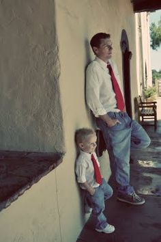 a man standing next to a little boy on the side of a building with his hands in his pockets