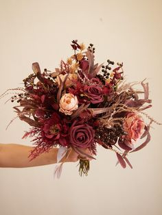 a person holding a bouquet of flowers in their hand with the background white wall behind them