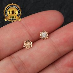 small gold plated flower stud earrings with clear cz crystals in the center, on a person's finger