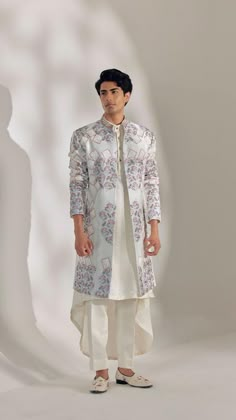 a man standing in front of a white background wearing a long coat and pants with floral designs on it