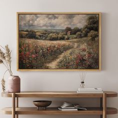 a painting hanging on the wall next to a wooden table and vase with flowers in it