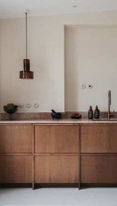 a large kitchen with wooden cabinets and marble counter tops, along with two hanging lights above the sink