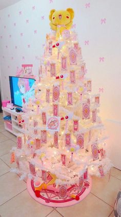 a white christmas tree decorated with pink and yellow decorations, teddy bear sitting on top