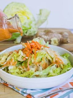 someone is pouring dressing into a salad in a bowl with lettuce and carrots