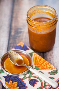 a jar of peanut butter next to a spoon on a colorful napkin with an orange flower design