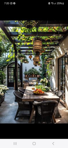 an outdoor dining area with potted plants on the table and hanging lights above it