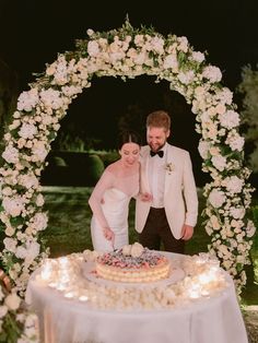 a bride and groom cutting their wedding cake at the end of an archway with white flowers