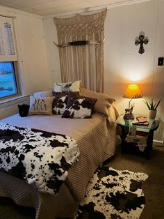 a cow print bed spread and pillows in a room with a window, rugs and lamp