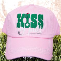 a pink hat with the words kiss my polo on it sitting in some green grass