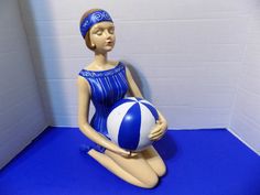 a female mannequin sitting on the floor with a ball in her hand and wearing a blue swimsuit