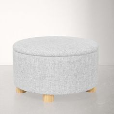 a grey ottoman with wooden legs on a white floor