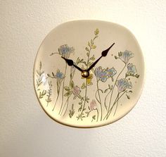 a clock with flowers painted on it hanging from the wall next to a white wall