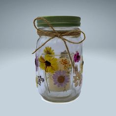 a glass jar with flowers painted on the inside and tied up to a green lid