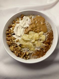 a white bowl filled with oatmeal, nuts and peanut butter on top