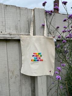 a tote bag hanging on the side of a wooden fence with purple flowers in front of it