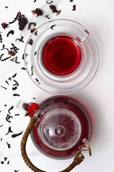 a glass cup filled with red liquid next to a tea strainer on a white surface