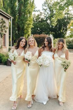 three bridesmaids in yellow dresses posing for the camera with their bouquets on