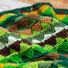 a crocheted blanket with green, brown and white designs on it's edges