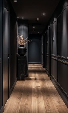 an empty hallway with dark walls and wooden floors is lit by recessed lights on either side