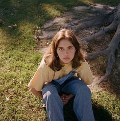 a young woman sitting on the ground next to a tree