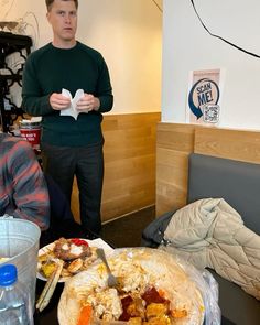 two men standing in front of a table with food and drinks on it, one holding a napkin