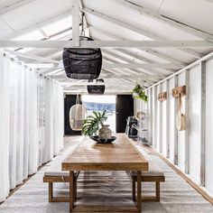 a dining room with a wooden table surrounded by white curtained walls and hanging plants