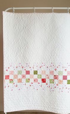 a white quilt hanging from a shower curtain with pink and green squares on the border