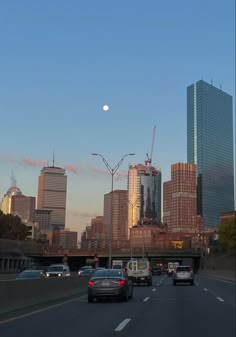 cars are driving down the highway in front of tall buildings and skyscrapers at sunset