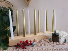 candles are lined up on a wooden stand with white and gold candles in the background