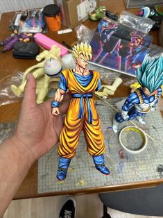 a hand is holding a dragon ball figurine in front of a table full of toys