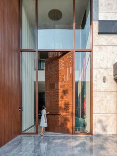 a woman standing in front of a wooden door on the side of a building with glass windows