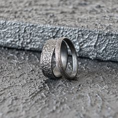 two silver rings sitting on top of a cement floor next to each other and one has a textured surface