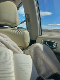 an open book sitting in the passenger seat of a car with a blanket on it