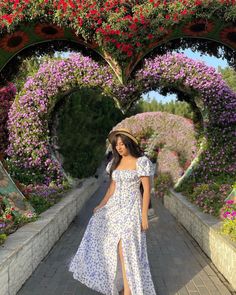 a woman in a dress and hat walking down a walkway with flowers all around her