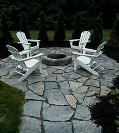 two white adironda chairs sitting on top of a stone patio next to a fire pit