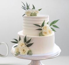 a three tiered cake with white flowers on top and greenery around the edges