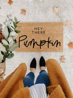 a person standing in front of a door mat that says hey there pumpkin