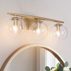 three clear globe lights are hanging on the wall above a mirror and vase with flowers