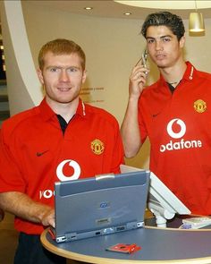 two men standing next to each other in front of a laptop computer on a table