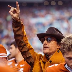 an old man in a cowboy hat and sunglasses on the sidelines at a football game