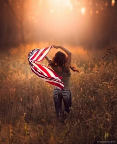 a woman holding an american flag in the middle of a field with sunbeams