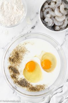 two eggs and some spices in bowls on a marble counter top with other ingredients to make the dish