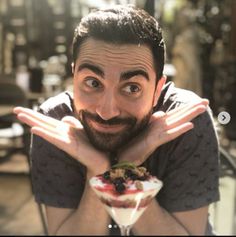 a man is holding his face up to the camera while eating an ice cream sundae