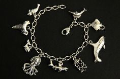 A collection of silver plated marine life themed charms have been dispersed around a shimmering silver plated bracelet chain in this handmade charm bracelet. This sea predator charm bracelet is then completed with a lobster clasp and a 1/2 inch of chain at the end for adjustable sizing. Charms in this bracelet include a seal charm, shark tooth charm, whale charm, octopus charm, shark charm, jellyfish charm, orca charm, stingray charm, and swordfish charm. ● Sizing ● To determine your bracelet si Ocean-inspired Silver Charms Jewelry, Handmade Silver Ocean-inspired Bracelets, Themed Silver Jewelry With Charms, Themed Bracelet With Lobster Clasp, Themed Jewelry With Lobster Clasp, Adjustable Silver Chain Bracelet With Dangling Charms, Silver Adjustable Chain Bracelet With Dangling Charms, Themed Silver Charm Bracelet, Themed Silver Jewelry With Dangling Charms