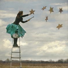 a woman is standing on a ladder and shooting stars in the sky