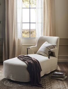 a white chair sitting in front of a window next to a brown blanket on top of a rug